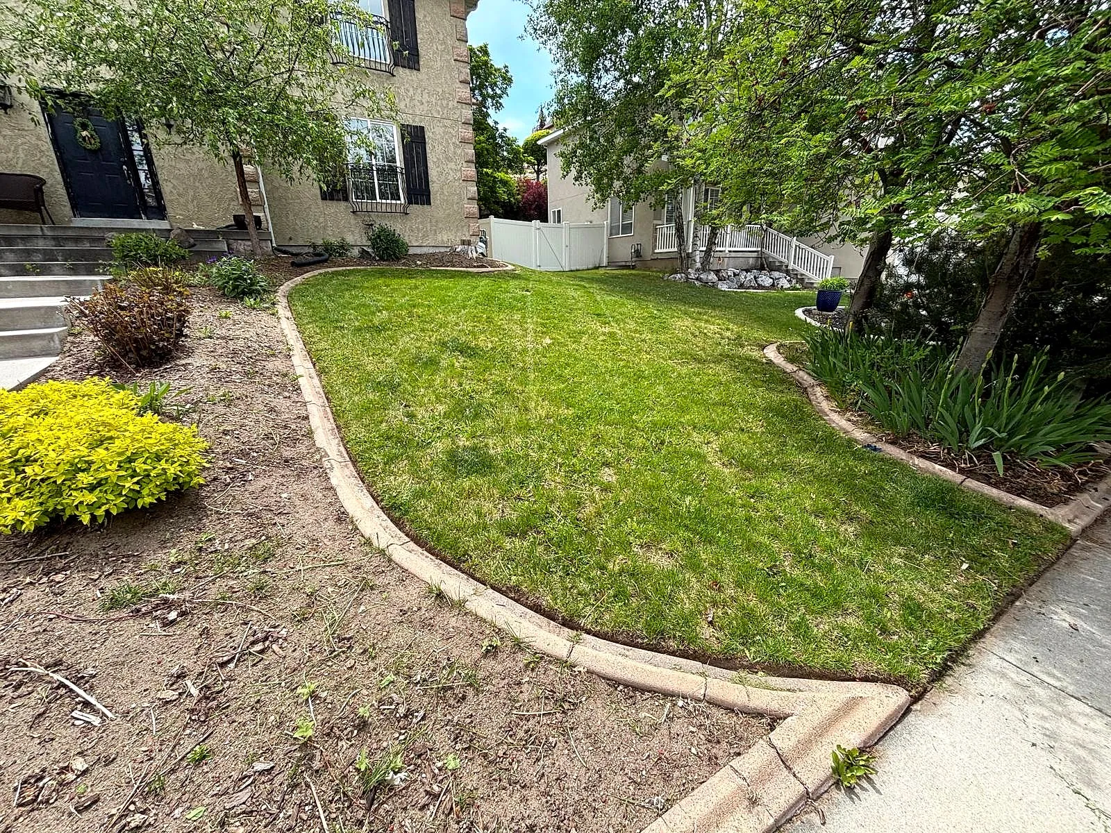 A curved lawn framed by a concrete border and planted beds, cared for by Taylor’d Lawn Care